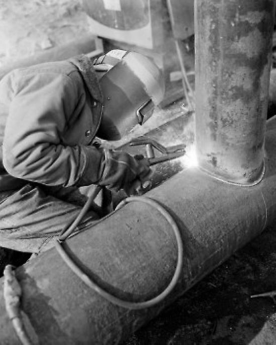 Man in welding mask welding pipe Poster