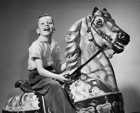 Boy riding on a carousel horse Poster